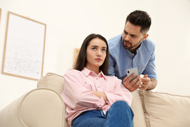 Photo of Young couple arguing about smartphone at home. Problems in relationship