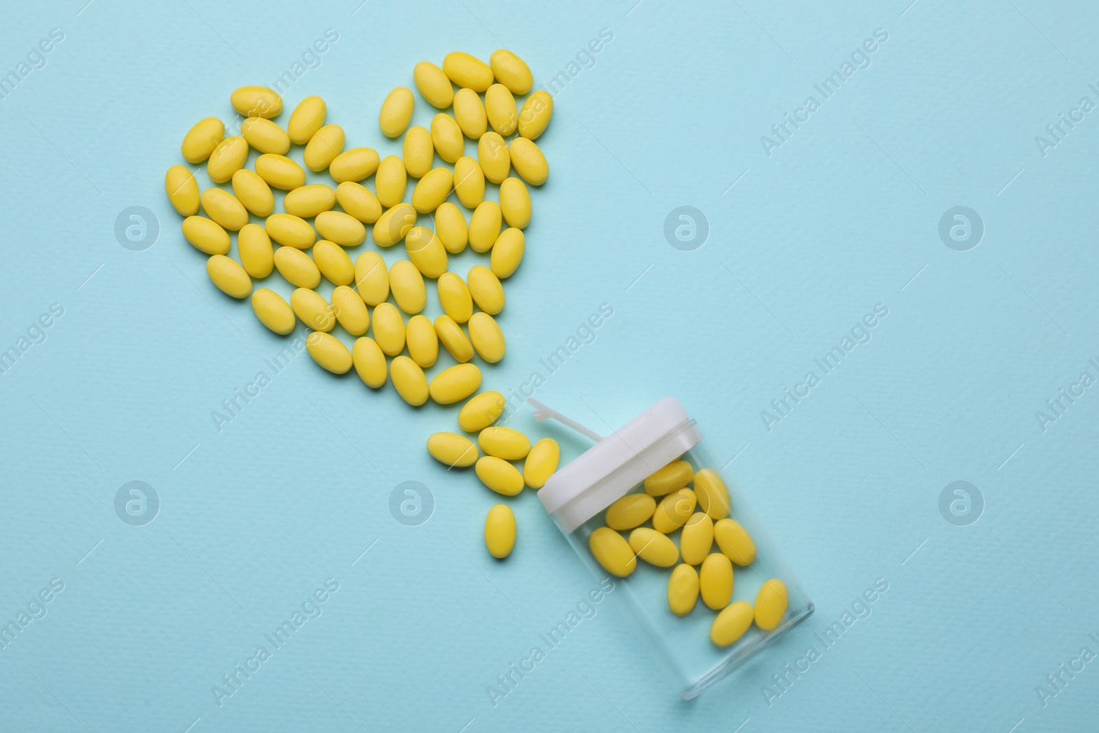 Photo of Heart made of yellow dragee candies and container on light blue background, flat lay