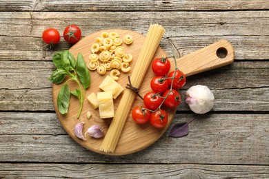 Photo of Board with different types of pasta and products on wooden table, flat lay