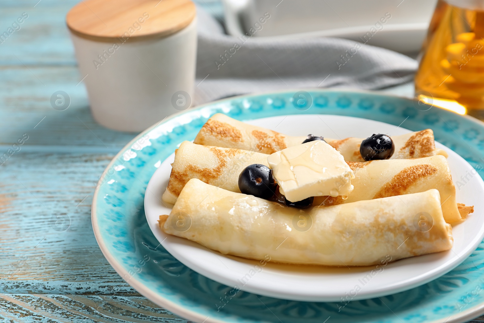 Photo of Thin pancakes with berries and butter on plate, closeup