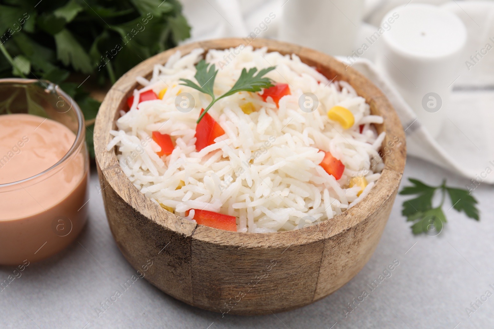 Photo of Bowl of delicious rice with vegetables and parsley on light table, closeup