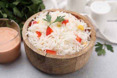 Photo of Bowl of delicious rice with vegetables and parsley on light table, closeup