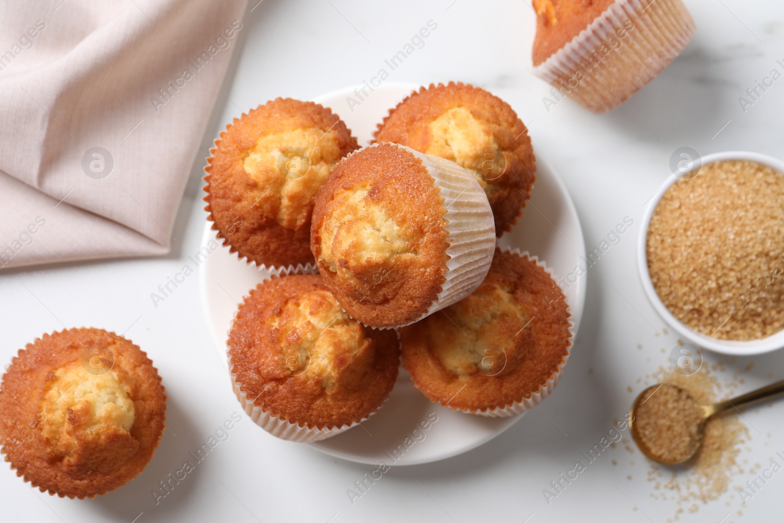 Photo of Delicious sweet muffins and brown sugar on white marble table, flat lay