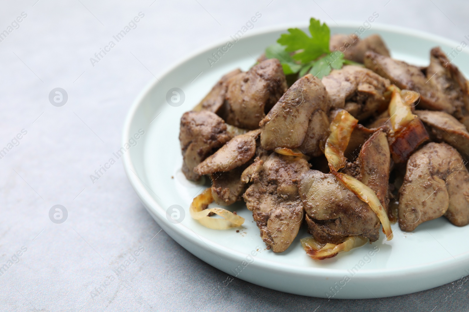 Photo of Tasty fried chicken liver with onion and parsley on grey table, closeup. Space for text