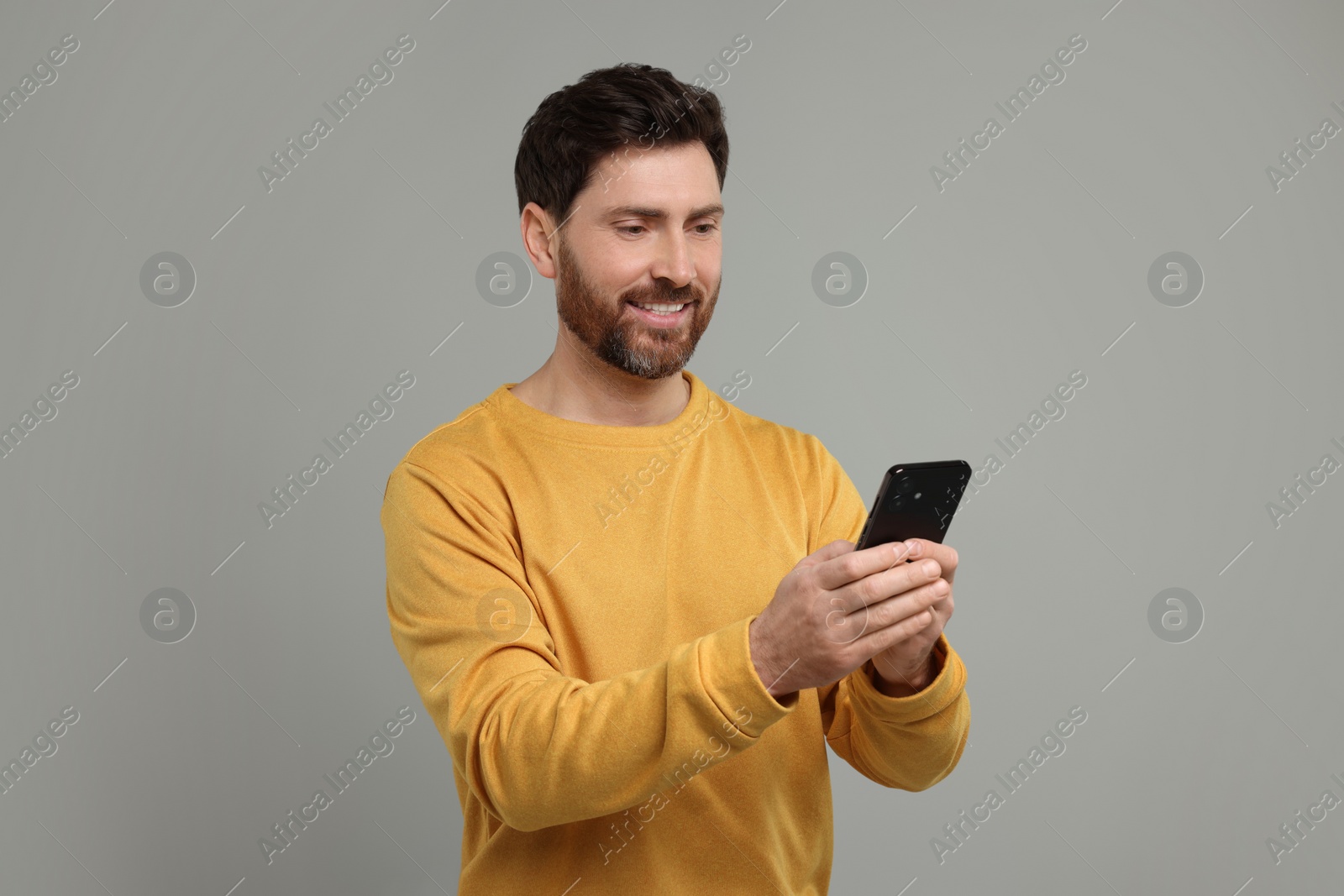 Photo of Smiling man with smartphone on grey background