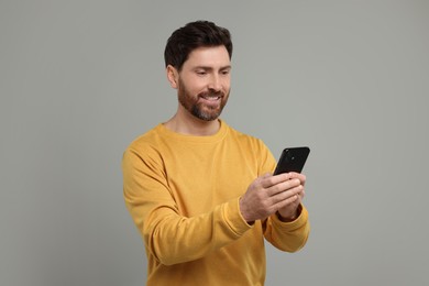 Smiling man with smartphone on grey background