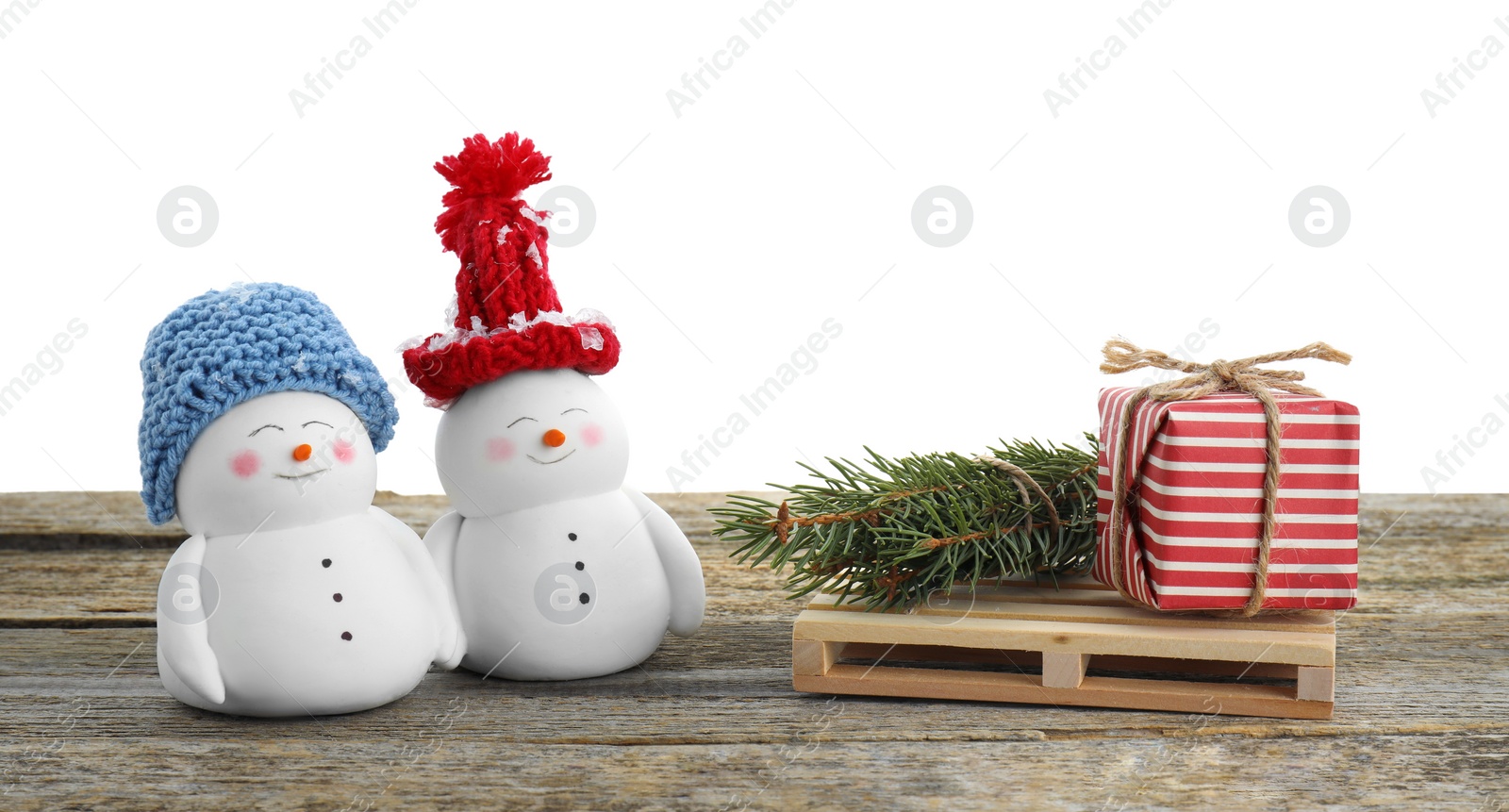 Photo of Cute decorative snowmen, gift box and fir tree branches on wooden table against white background