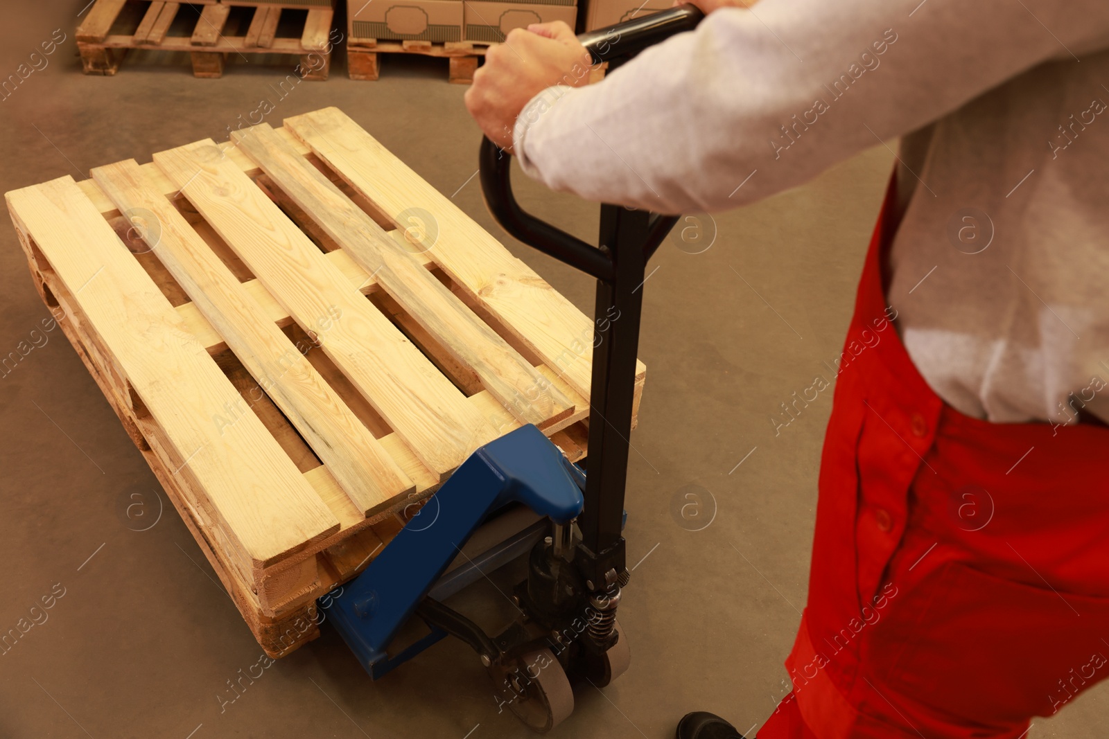 Image of Worker moving wooden pallets with manual forklift in warehouse, closeup