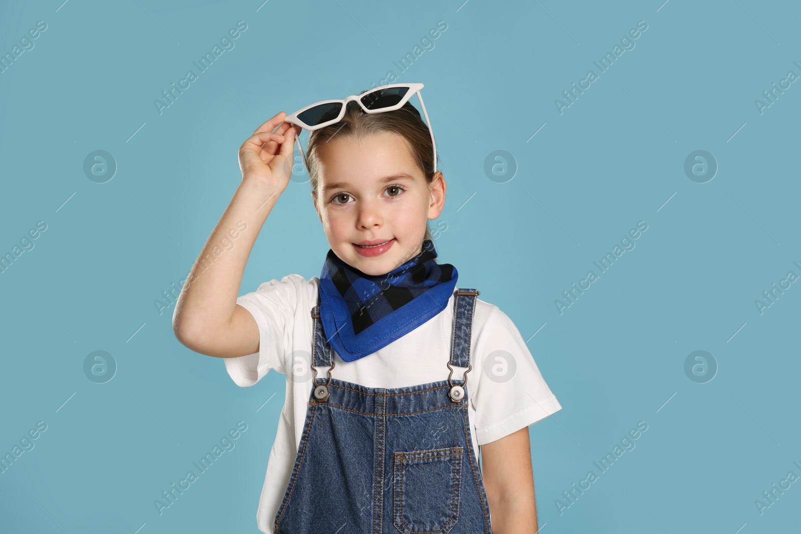 Photo of Cute little girl wearing stylish bandana and sunglasses on turquoise background