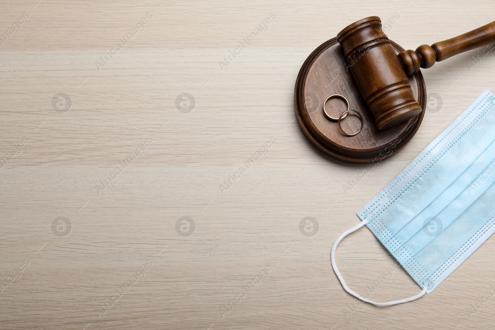 Photo of Gavel, protective mask and wedding rings on wooden table, flat lay with space for text. Divorce during coronavirus quarantine