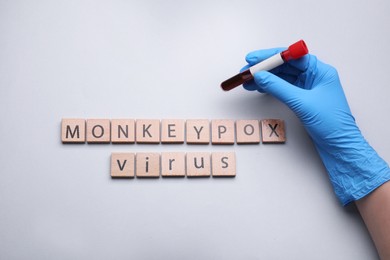 Photo of Nurse holding test tube and words Monkeypox Virus made of wooden cubes on white background, top view