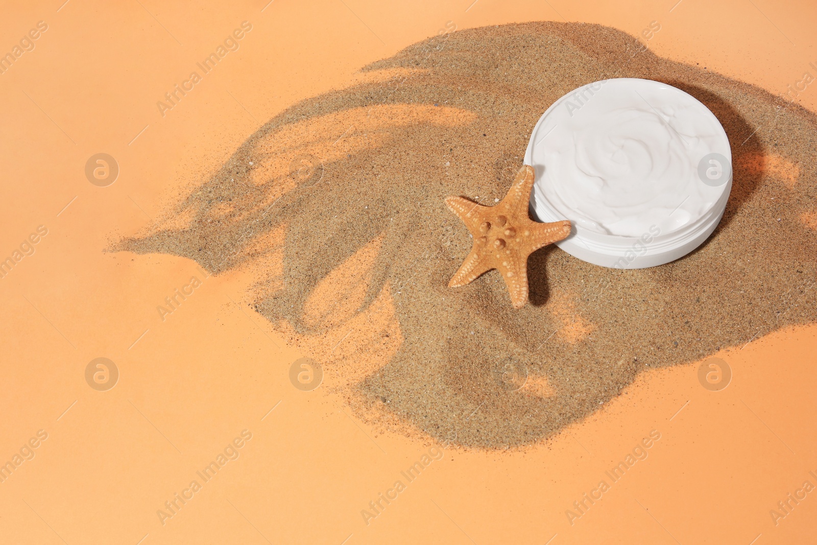 Photo of Jar with cream and starfish on sand against orange background, above view with space for text. Cosmetic product