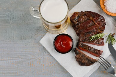 Mug with beer, fried steak and sauce on grey wooden table, flat lay. Space for text