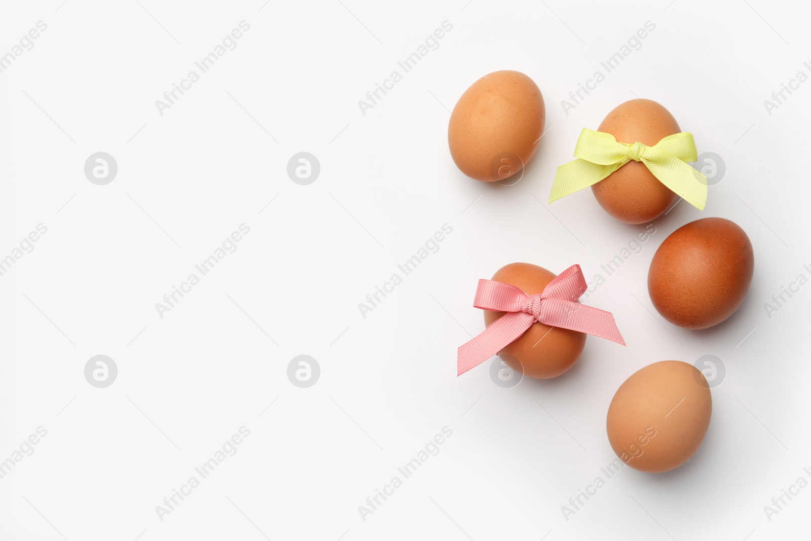 Photo of Easter eggs with colorful bows on white background, flat lay. Space for text