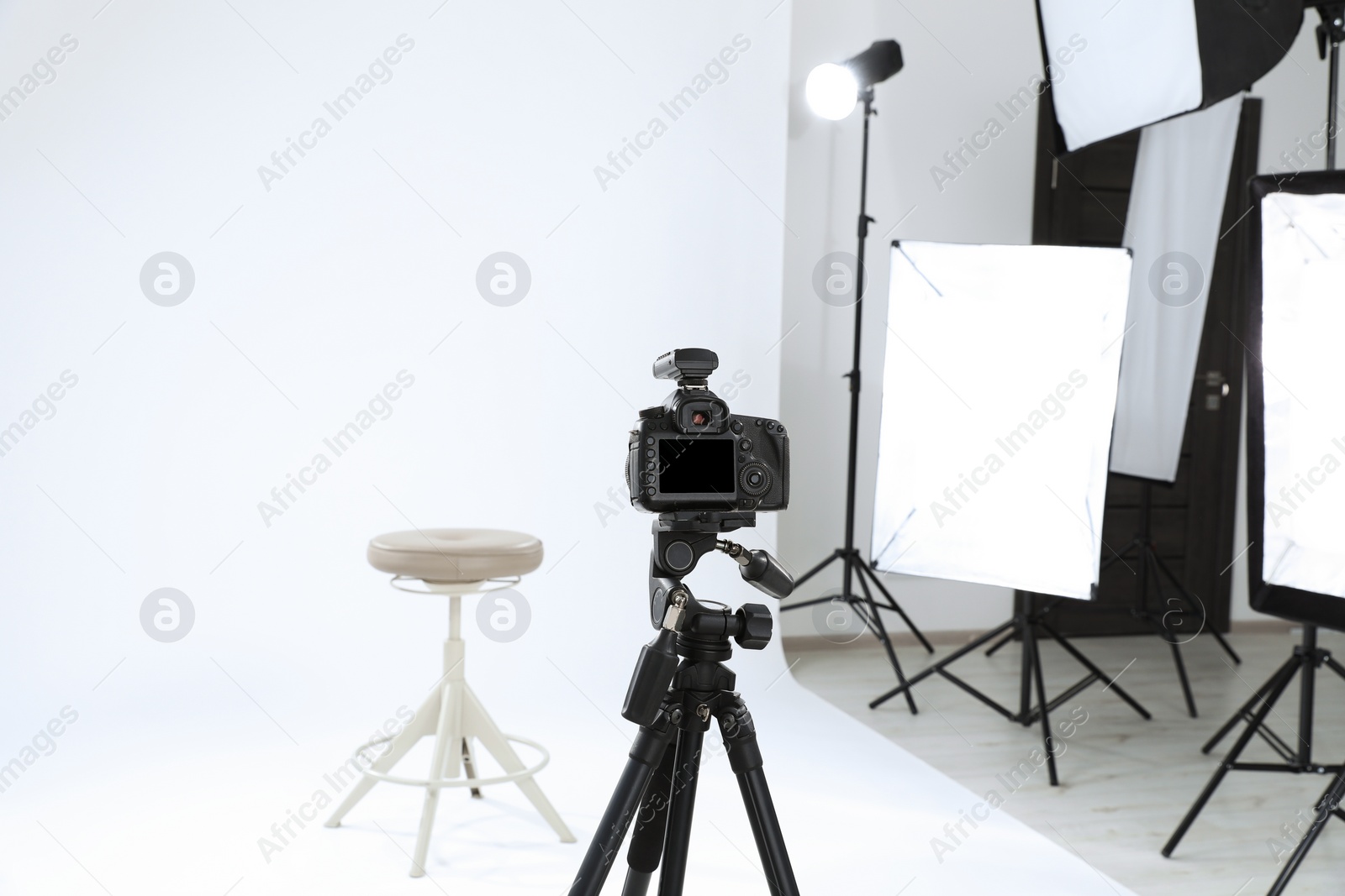 Photo of Tripod with camera, bar stool and professional lighting equipment in modern photo studio