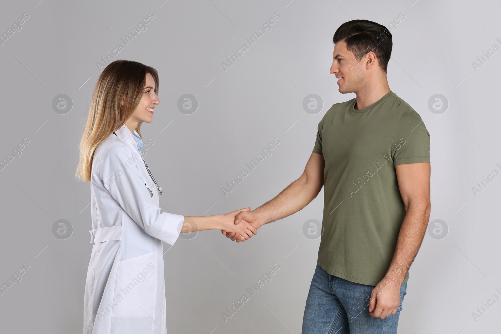 Photo of Doctor and patient shaking hands on light grey background