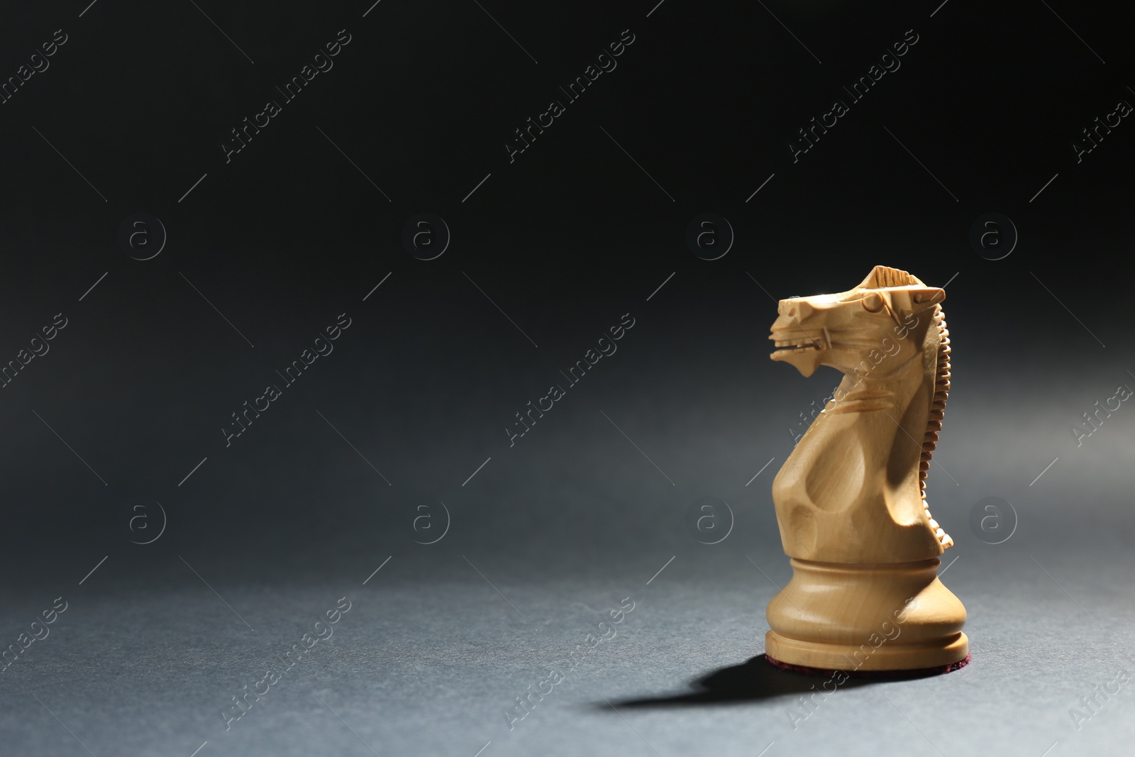 Photo of White wooden chess knight on dark background. Space for text