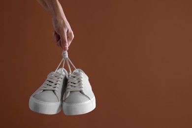 Man holding stylish sneakers on brown background, closeup. Space for text