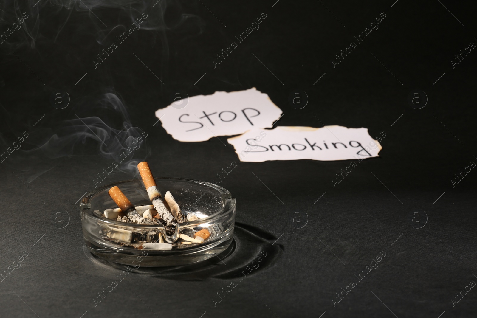 Photo of Ashtray with burnt cigarettes and words Stop Smoking written on paper on black table