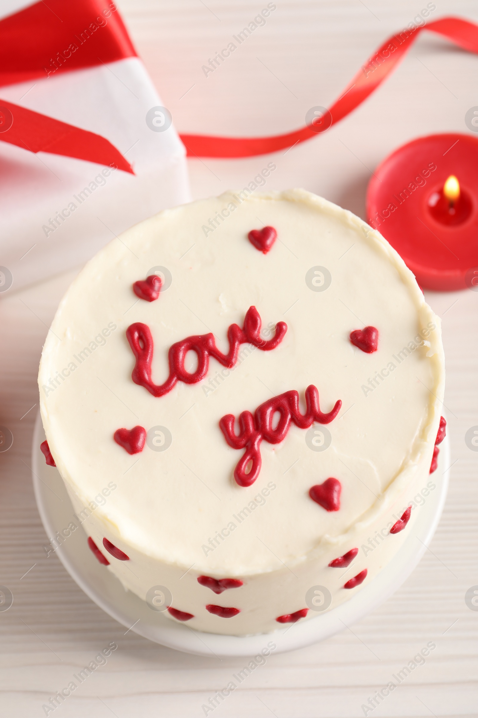 Photo of Bento cake with text Love You, candle and gift box on white wooden table, above view. St. Valentine's day surprise