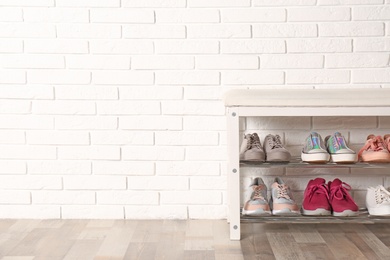 Photo of Shoe storage bench with different sneakers near brick wall, space for text