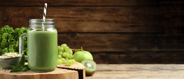 Mason jar of fresh green smoothie and ingredients on wooden table, space for text. Banner design