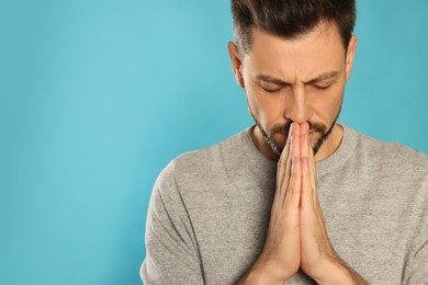 Photo of Man with clasped hands praying on turquoise background. Space for text