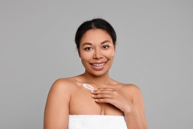 Photo of Young woman applying cream onto body on grey background