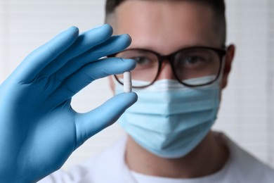 Photo of Doctor holding pill on light background, selective focus. Space for text