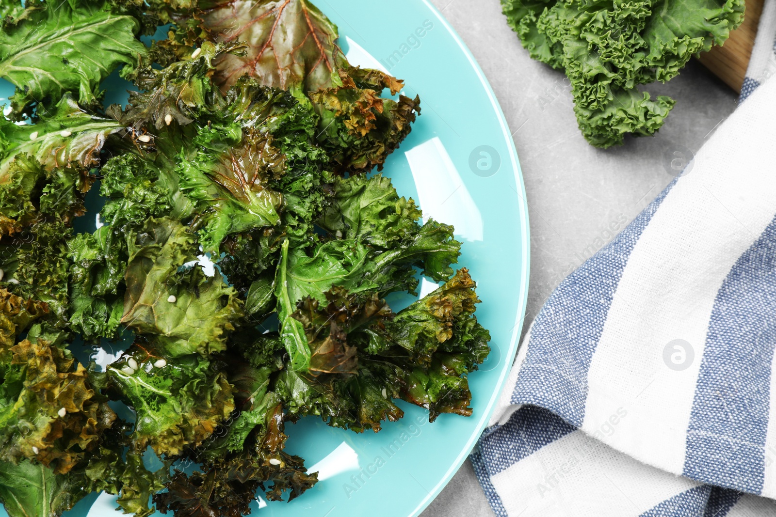 Photo of Tasty baked kale chips on light grey table, flat lay