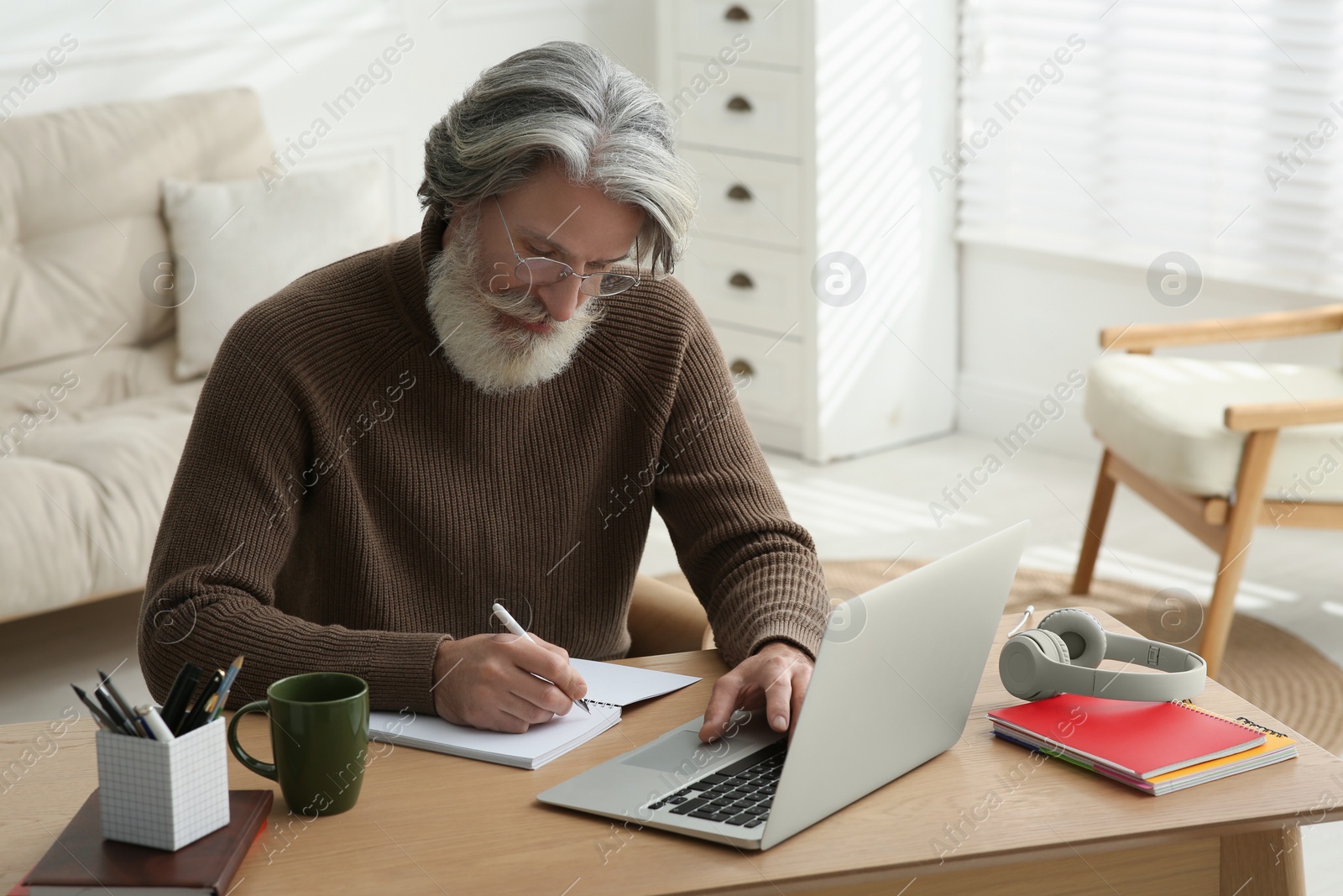 Photo of Middle aged man with laptop and notebook learning at table indoors