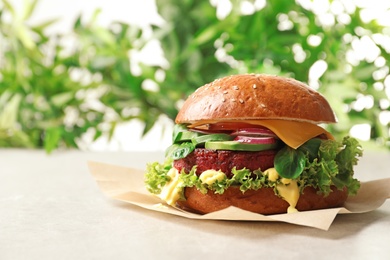 Photo of Tasty vegetarian burger with beet cutlet on table against blurred background. Space for text
