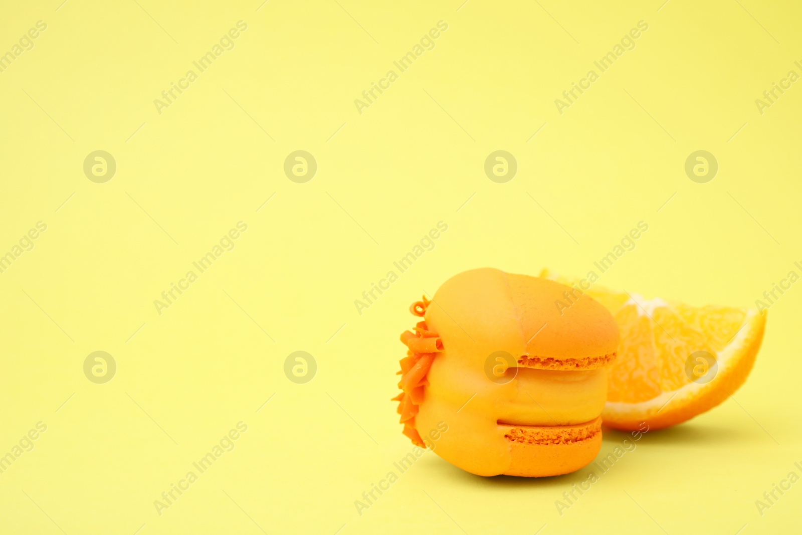 Photo of Delicious macaron and orange slice on yellow background, closeup. Space for text