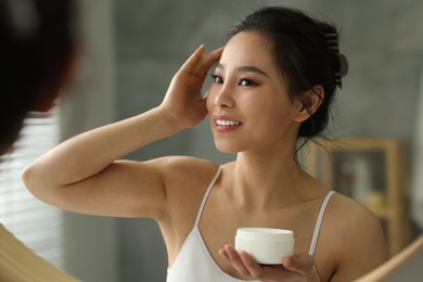 Photo of Happy woman applying face cream near mirror at home