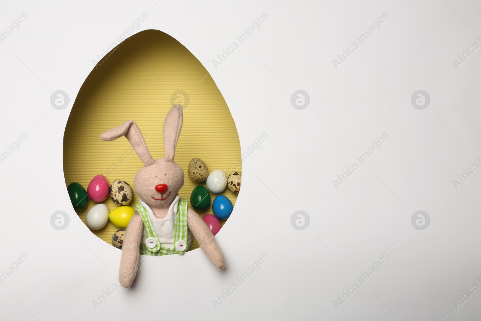 Photo of View of composition with Easter bunny toy on color background through egg shaped hole, top view. Space for text