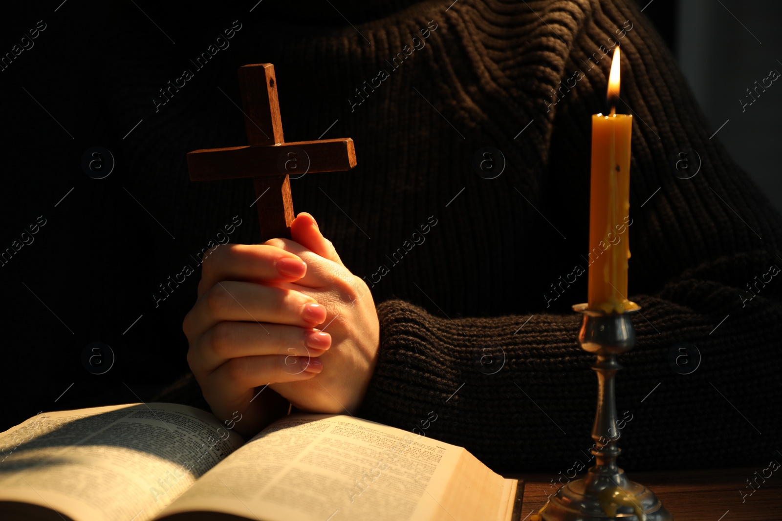 Photo of Woman praying at table with burning candle and Bible, closeup