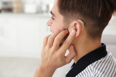 Photo of Young man adjusting hearing aid at home, closeup