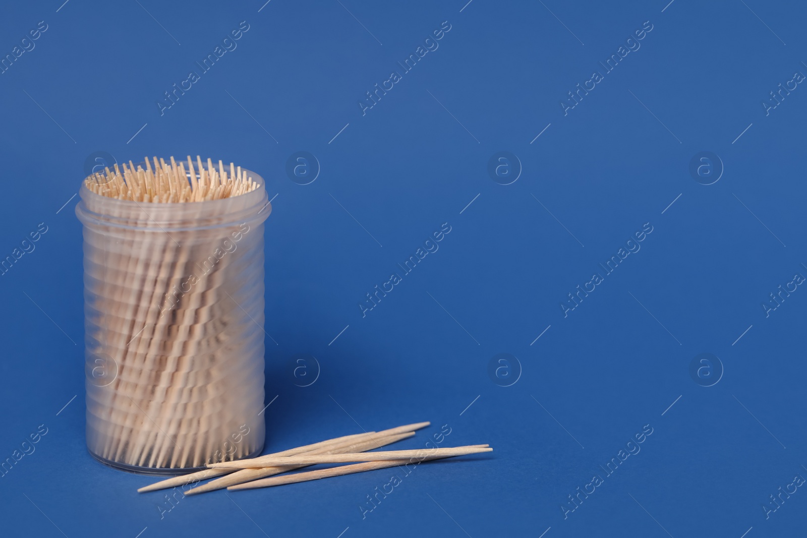 Photo of Wooden toothpicks and holder on blue background. Space for text