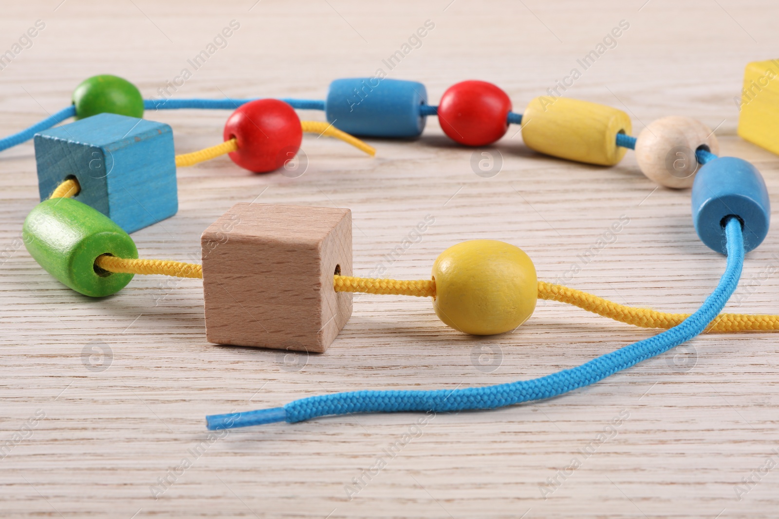 Photo of Wooden pieces and string for threading activity on light table, closeup. Motor skills development