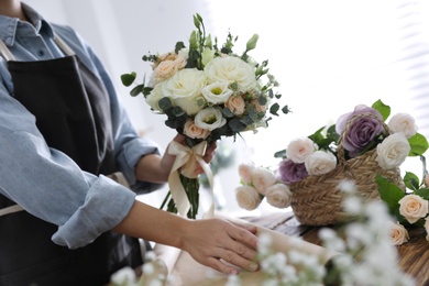 Photo of Florist making beautiful wedding bouquet at wooden table, closeup