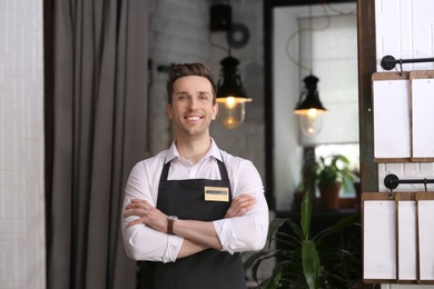 Young waiter in apron at workplace