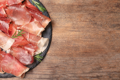 Photo of Pile of tasty prosciutto on wooden table, top view. Space for text