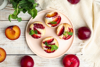 Delicious cupcakes with plums on white wooden table, flat lay