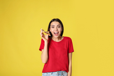 Emotional woman with tasty pizza on yellow background