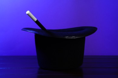 Photo of Black top hat and wand on wooden table. Magician equipment