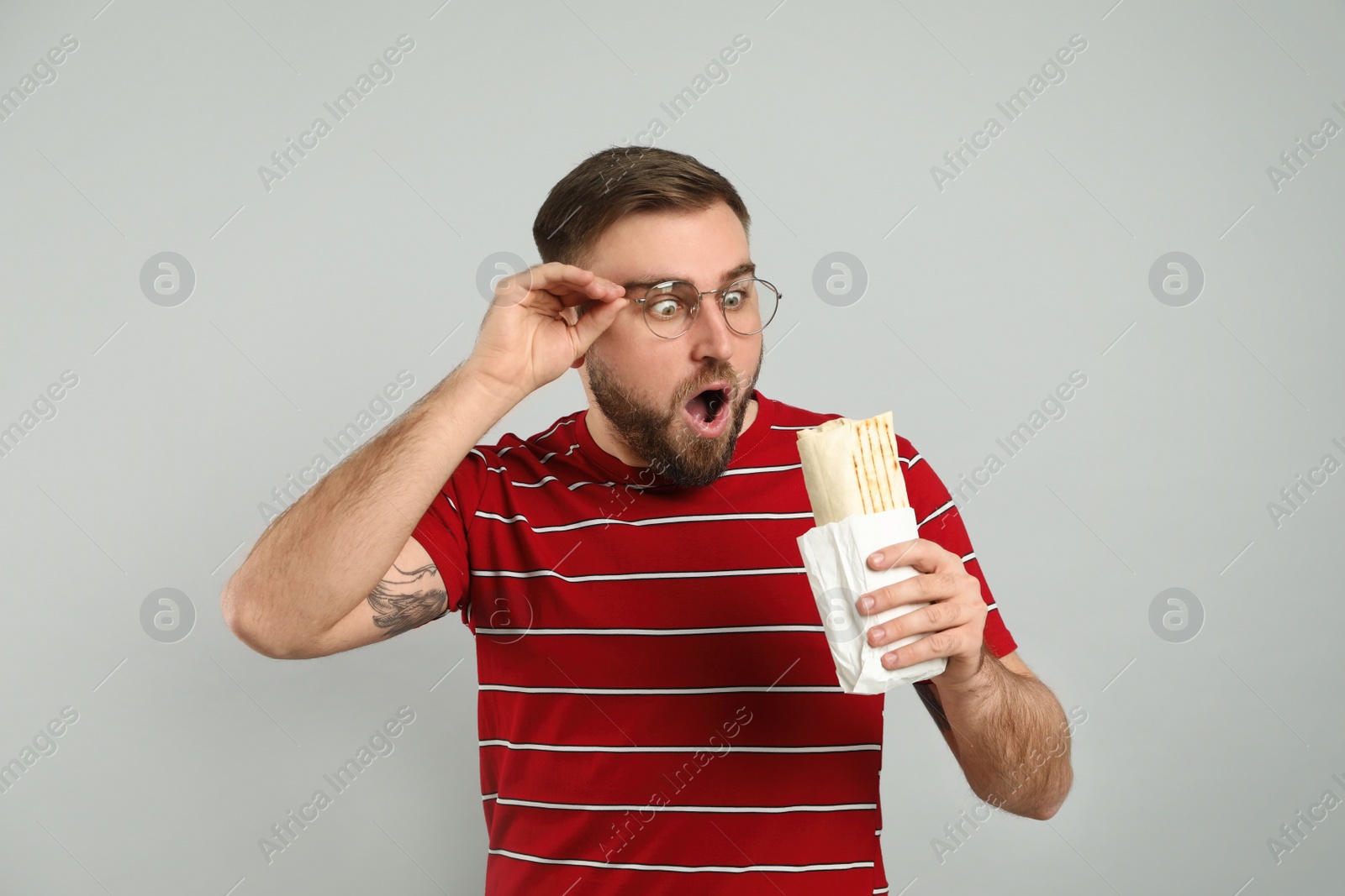 Photo of Emotional young man with delicious shawarma on grey background