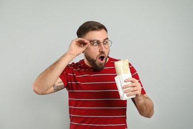 Emotional young man with delicious shawarma on grey background