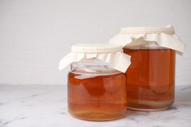 Photo of Tasty kombucha in glass jars on white marble table, space for text