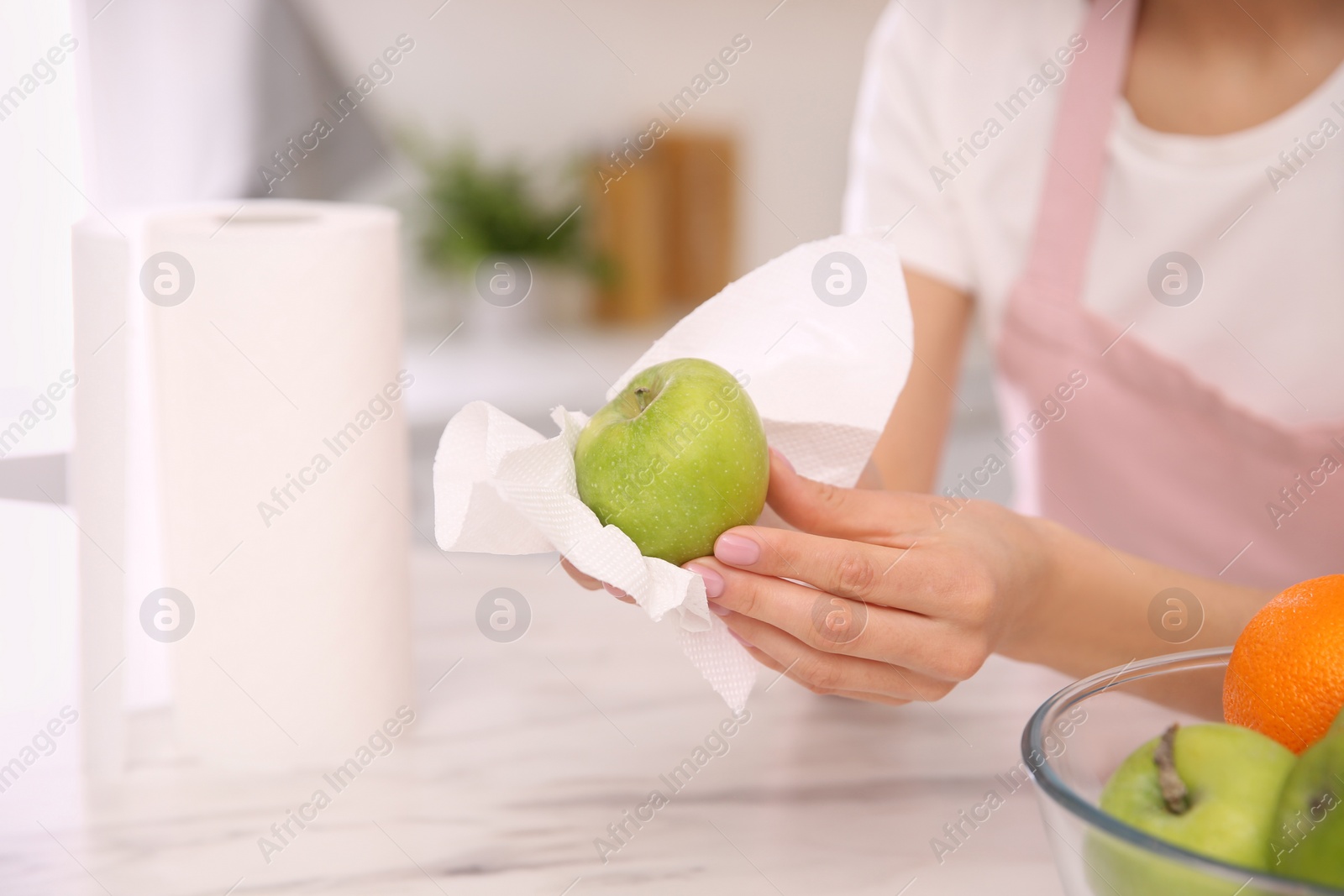 Photo of Woman wiping green apple with paper towel in kitchen, closeup