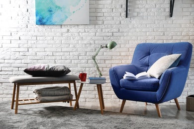 Room interior with comfortable furniture and books near brick wall